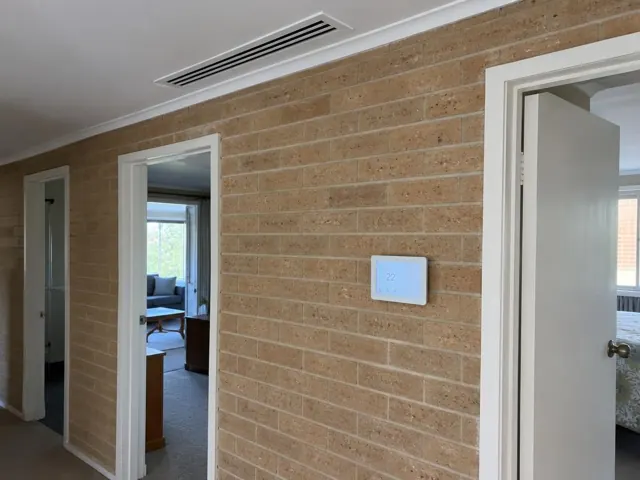 Ceiling return grille and wall zone controller in a brick hallway with white doors in Elizabeth North