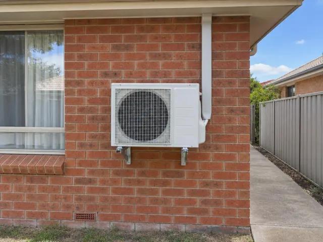 Outdoor air conditioner unit mounted on brick wall beside a side path in a suburban house in Munno Para